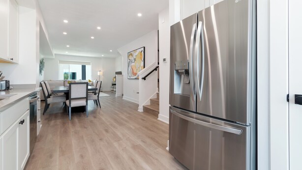 A modern kitchen with a stainless steel refrigerator, wooden flooring, and a dining area with a table and chairs. - 3 Bed Brand NEW Townhome in Downtown Grand Junction! NO EXTRA FEES! (Grand Junction)