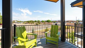 A balcony with two green Adirondack chairs, a wooden ceiling, and a view of a parking lot and distant buildings. - 3 Bed Brand NEW Townhome in Downtown Grand Junction! NO EXTRA FEES! (Grand Junction)