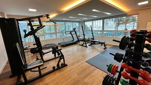 Un gimnasio con máquinas de cardio, equipo de levantamiento de pesas y grandes ventanales con vistas al exterior.