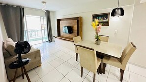 Una sala de estar moderna con comedor, un sofá, un ventilador y un televisor montado en una pared de madera.