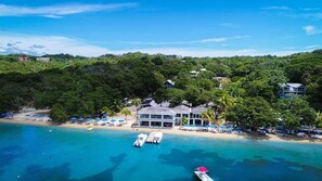 Un complejo turístico costero con un edificio grande, playa y aguas azules cristalinas.