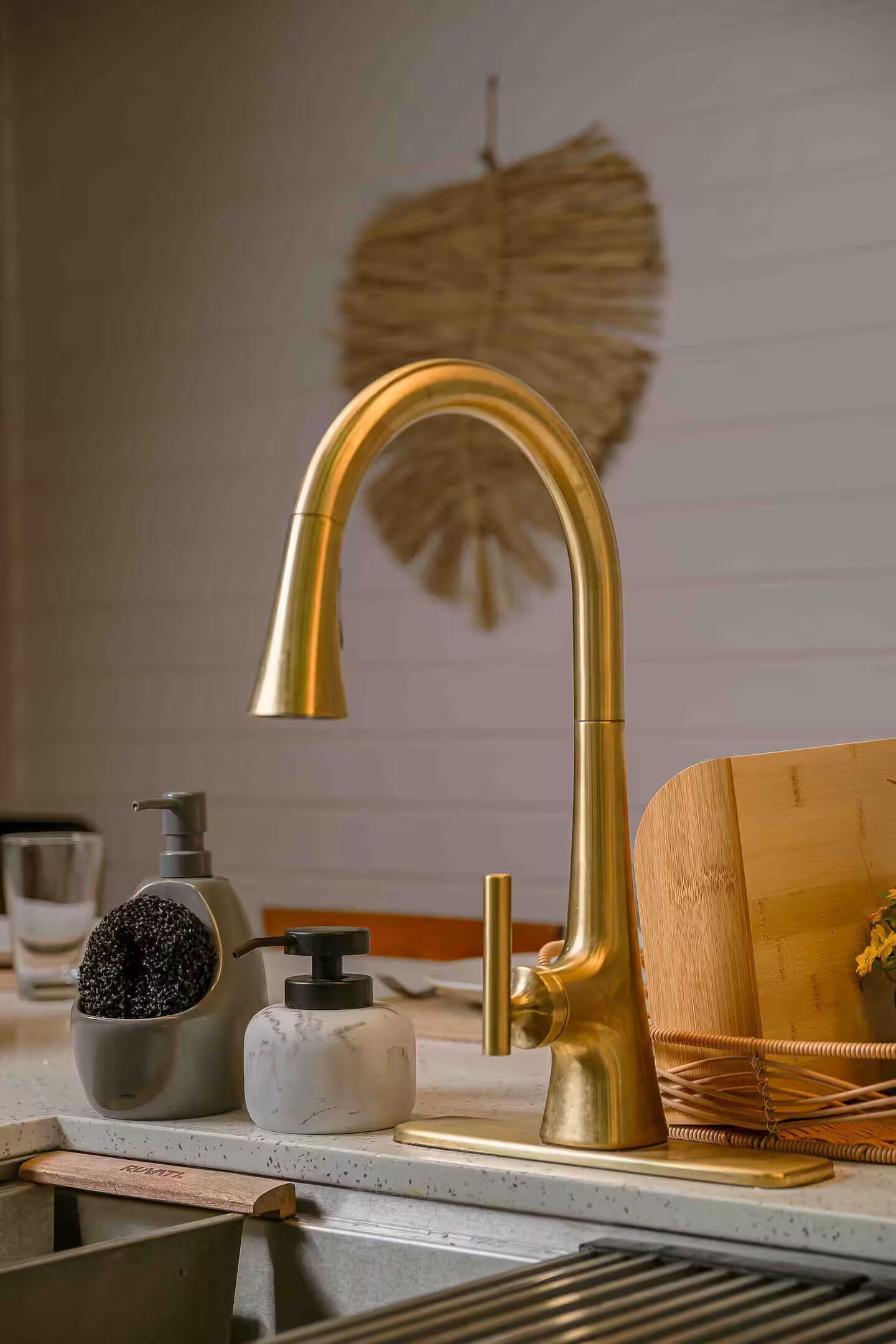 A kitchen with a gold faucet, a soap dispenser, and a wooden cutting board.