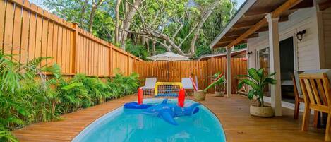 A wooden deck with a swimming pool, surrounded by a wooden fence and lush greenery.