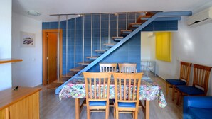 Ein Essbereich mit Treppe, Holzsesseln, einem Tisch mit floralem Tischläufer und einer gelben Wand.