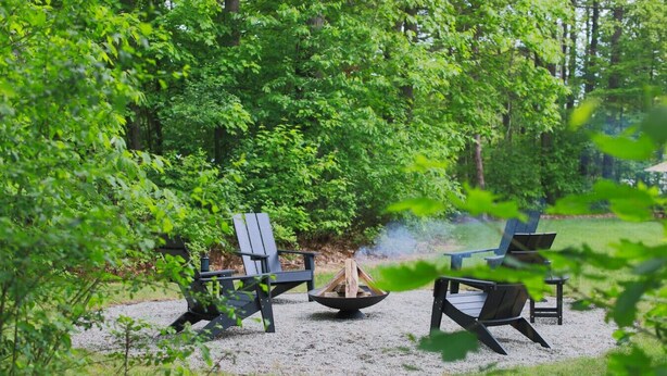 A campsite with three Adirondack chairs arranged around a central fire pit, surrounded by dense forest. - The Green Mountain Escape ~ Near Trails & Lake (Colchester)