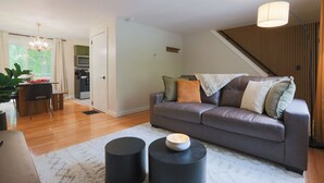 A modern living room with a grey sofa, black cylindrical side tables, and a staircase in the background. - The Green Mountain Escape ~ Near Trails & Lake (Colchester)