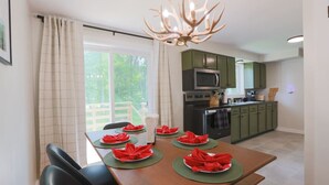 A dining area with a wooden table set for four, green placemats, and a chandelier. - The Green Mountain Escape ~ Near Trails & Lake (Colchester)