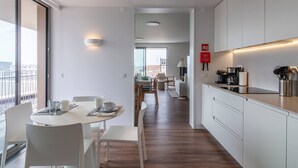 A modern kitchen with white cabinets, a dining area with a round table and chairs, and a view of the city through large windows. - URBAN PENTHOUSE by Azores HomeMade (Ponta Delgada)