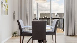 A dining area with a round table and two chairs, a pendant light, and a view of a residential building through large glass doors. - Luxury 5BR House for Large Groups & Families | Cozy Home in Calgary (Calgary)