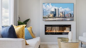 A modern living room with a white sofa, colorful cushions, a fireplace, and a cityscape painting. - Luxury 5BR House for Large Groups & Families | Cozy Home in Calgary (Calgary)
