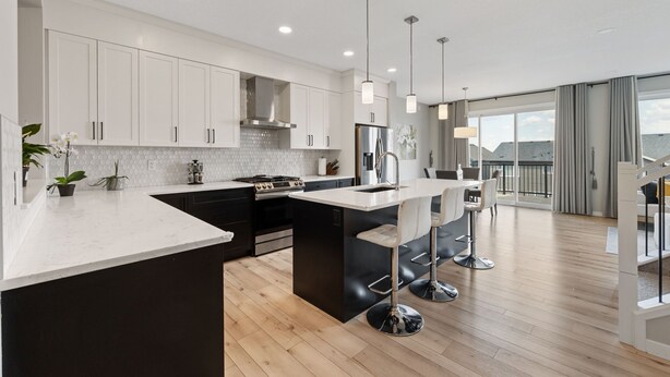 A modern kitchen with white cabinets, a central island with bar stools, and a view of the balcony. - Luxury 5BR House for Large Groups & Families | Cozy Home in Calgary (Calgary)
