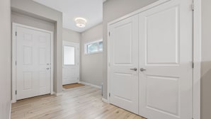A hallway with two white doors, wooden flooring, and a small window. - Luxury 5BR House for Large Groups & Families | Cozy Home in Calgary (Calgary)