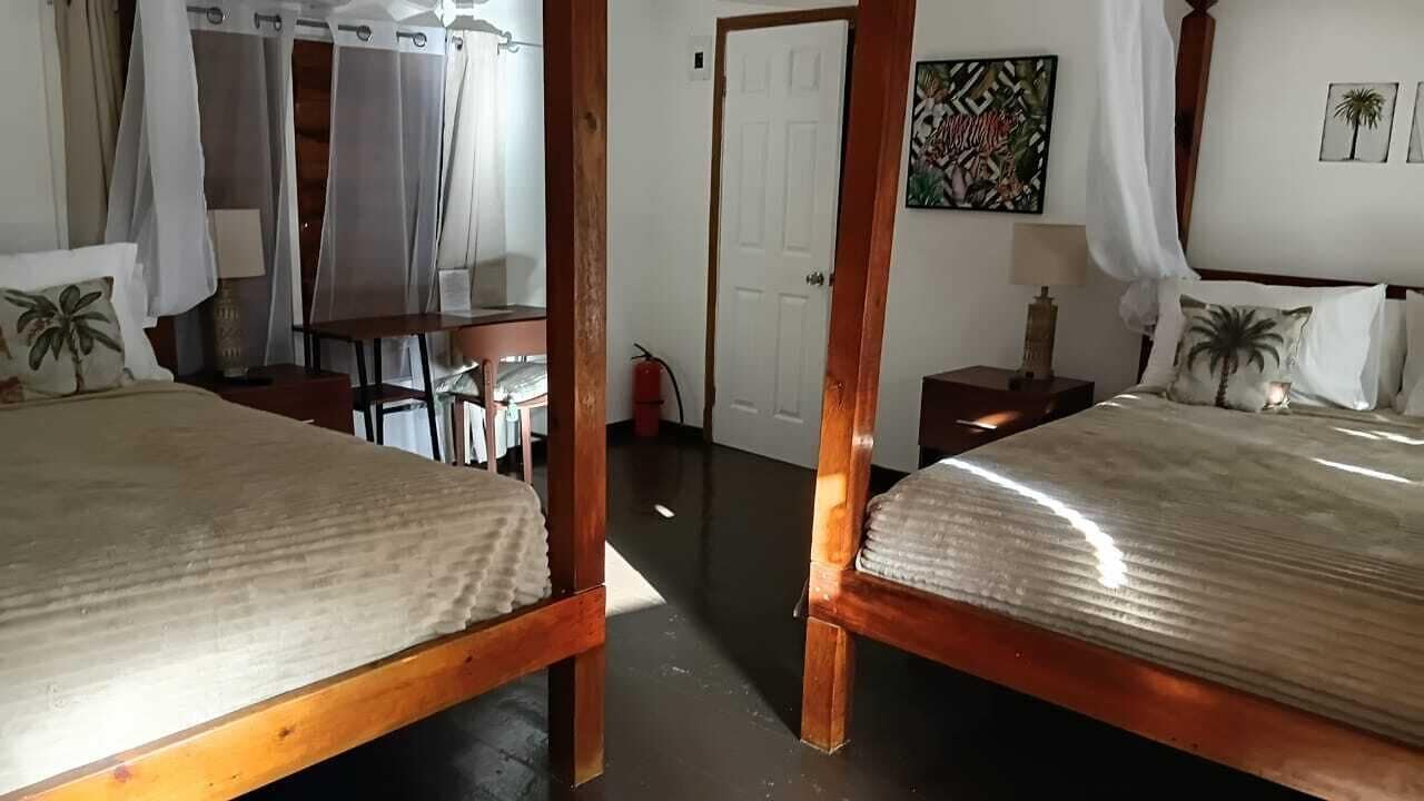 Una habitación con dos camas, un escritorio, una silla, una puerta y una pared con un cuadro.