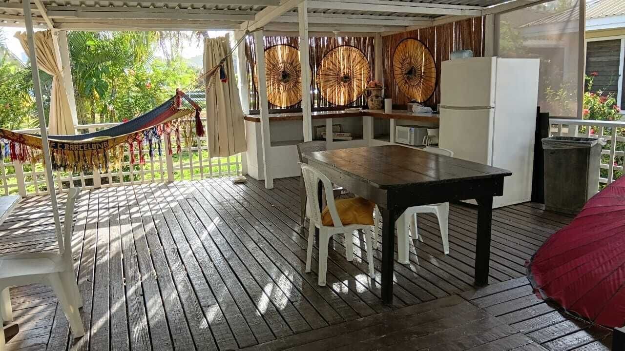 A wooden deck with a table and chairs, a hammock, and a view of greenery.