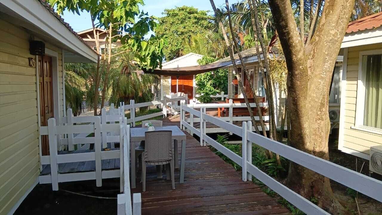Una terraza de madera con una valla blanca, una mesa con sillas y un área techada.