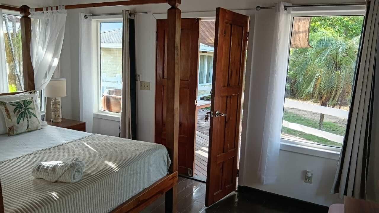 A bedroom with a four-poster bed, a wooden door, and a view of the outside.
