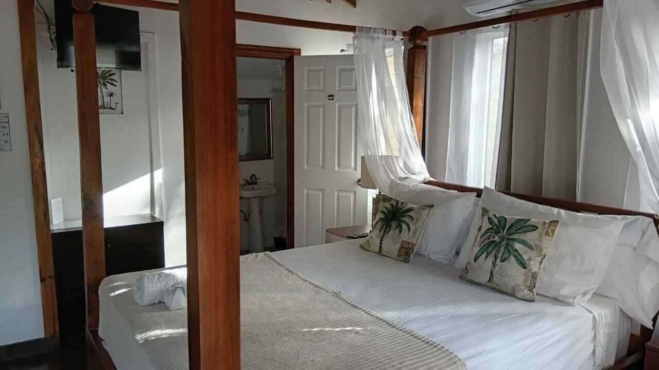Een slaapkamer met een hemelbed, nachtkastje, spiegel en deur naar een badkamer.
