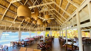 An open-air restaurant with wooden tables and chairs, hanging baskets, and a view of the sea. - Las Palmas Cabins (Dixon Cove)