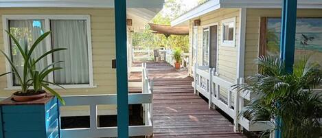A covered wooden deck leading to a row of cabins with windows and potted plants.