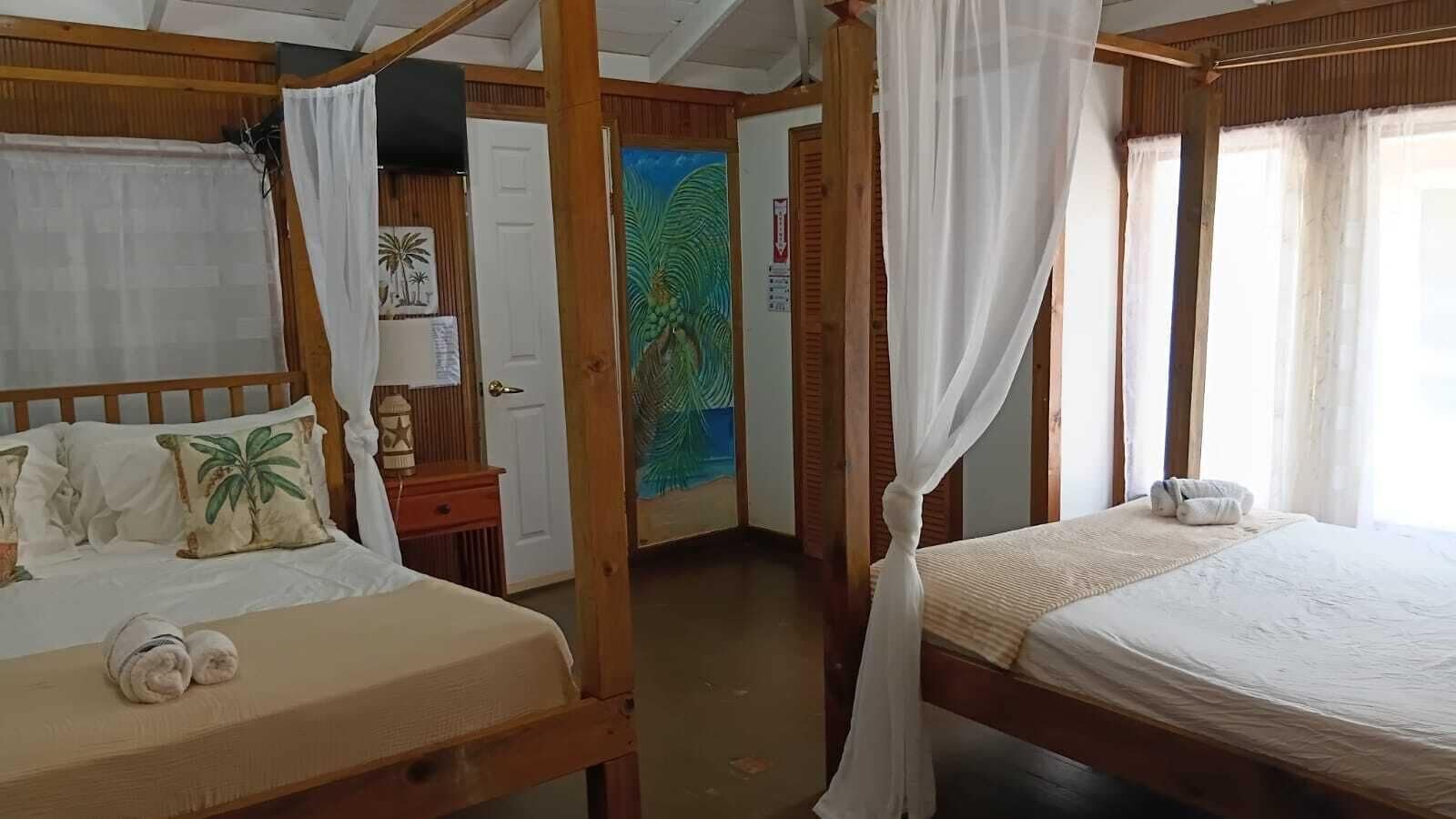 Una stanza con due letti di legno, ciascuno con baldacchino, un piccolo tavolo con una lampada e una porta che conduce a un'altra stanza con un affresco.