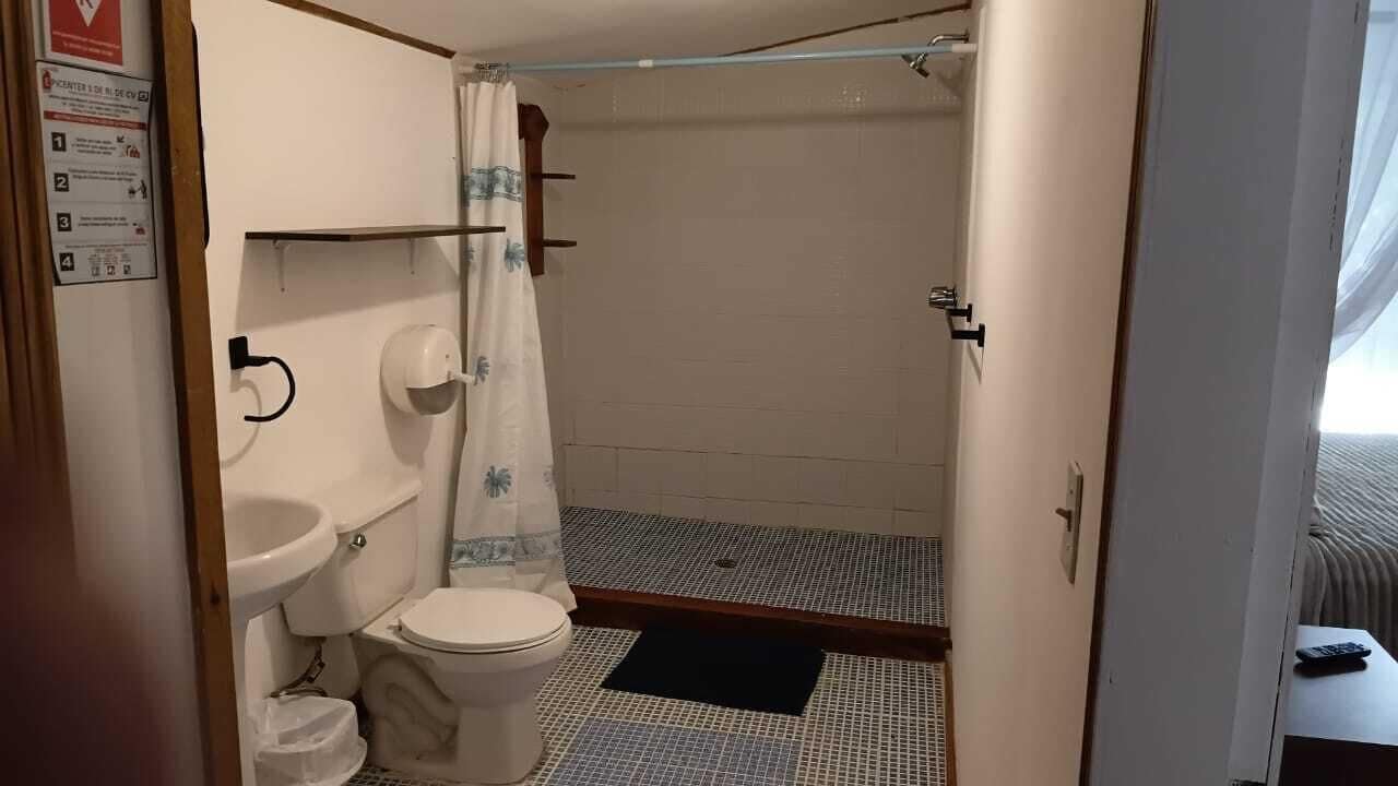 A bathroom with a toilet, sink, shower, and a black mat.