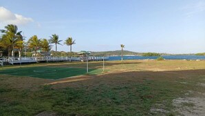 A beach area with a tennis court, palm trees, a bridge, and a view of the ocean. - Las Palmas Cabins (Dixon Cove)