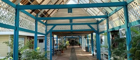 A covered wooden deck with a blue lattice structure, potted plants, and a central pathway.