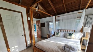 A four-poster bed with a canopy, wooden flooring, a door, and a nightstand with a lamp. - Las Palmas Cabins (Dixon Cove)