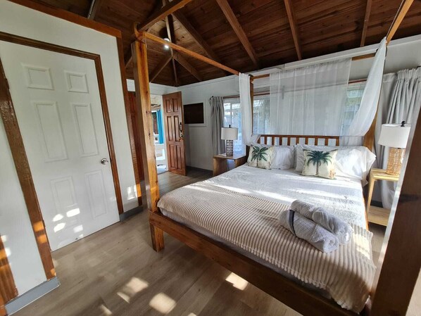 A four-poster bed with a canopy, wooden flooring, a door, and a nightstand with a lamp. - Las Palmas Beach Roatan (Dixon Cove)