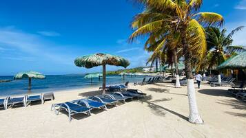 A beach with lounge chairs, palm trees, and umbrellas.