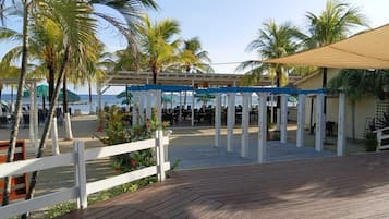 A wooden deck with a white fence, palm trees, and a covered area with tables and chairs.