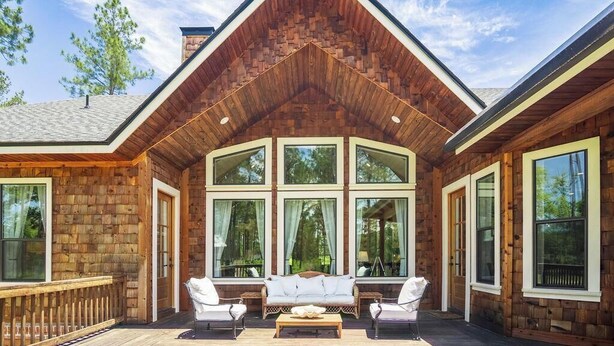 Une cabane en rondins dotée d’une grande véranda, de nombreuses fenêtres et d’un toit en bois.