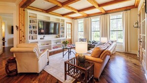 Un salon spacieux avec un grand canapé d’angle, un meuble de rangement blanc pour les appareils électroniques et un plafond en bois.