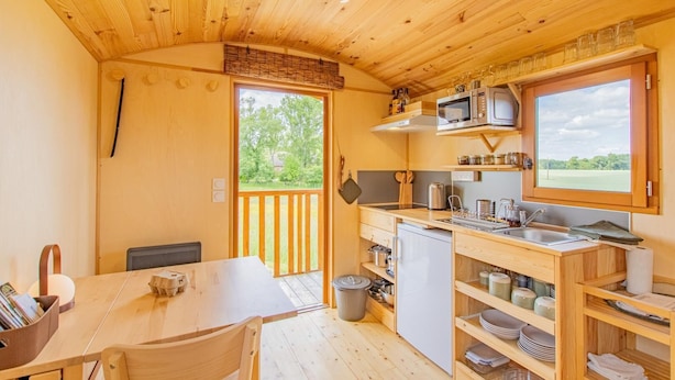 A compact kitchen with wooden cabinets, a microwave, and a window overlooking a green landscape. - La P'tiote Roulotte - MOUTHIER EN BRESSE (MOUTHIER EN BRESSE)