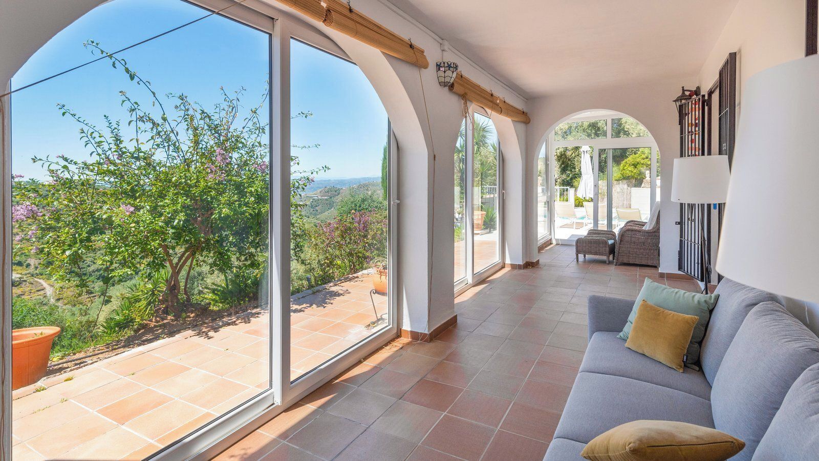 Ein geräumiger Wohnbereich mit großen Fenstern, einem grauen Sofa und Blick auf einen Garten.
