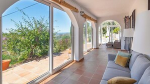 A spacious living area with large windows, a grey sofa, and a view of a garden.