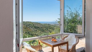 A balcony with wicker furniture, a table with fruit, and a view of a green landscape.