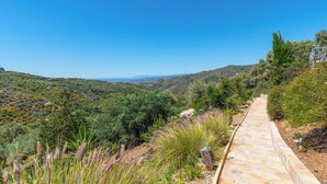 A stone pathway leading through a lush, green landscape with distant hills and a clear blue sky.