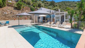 A swimming pool with lounge chairs and umbrellas, surrounded by a stone wall and vegetation.