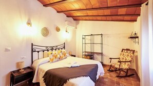 A bedroom with a bed, a chair, a shelf, and a hanging light fixture.