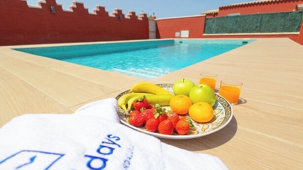 A poolside table with a plate of fruit and a glass of orange juice, a towel, and a pool in the background. - Casa Álvaro Conil Conil de la Frontera by Ruralidays (Cádiz)