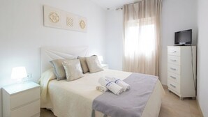 A neatly arranged hotel room with a bed, a nightstand with a lamp, a dresser, and a television. - Casa Álvaro Conil Conil de la Frontera by Ruralidays (Cádiz)