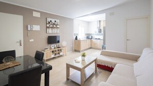 A modern living room with a glass dining table, a sofa, and a kitchen in the background. - Casa Álvaro Conil Conil de la Frontera by Ruralidays (Cádiz)