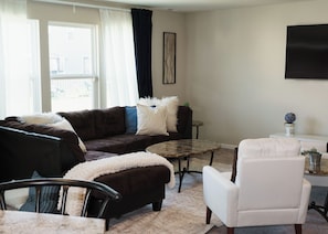 A living room with a dark brown sofa, a white armchair, a glass coffee table, and a small side table with a decorative item.