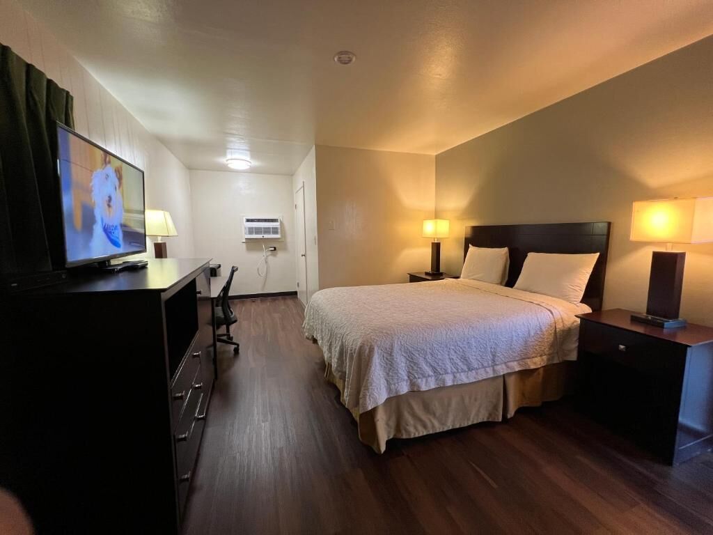 A hotel room with a bed, bedside lamps, a TV, a desk, and a chair.