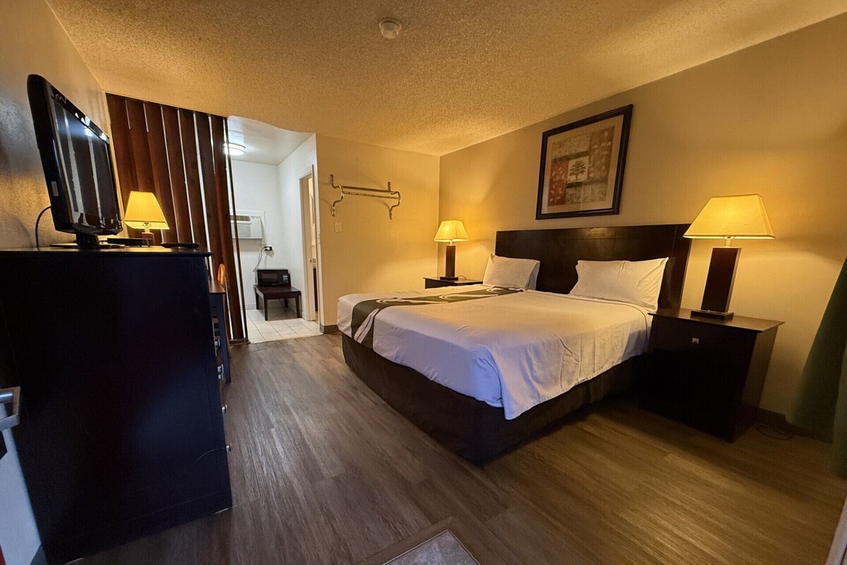 A hotel room with a bed, bedside lamps, a desk with a computer, and a television.