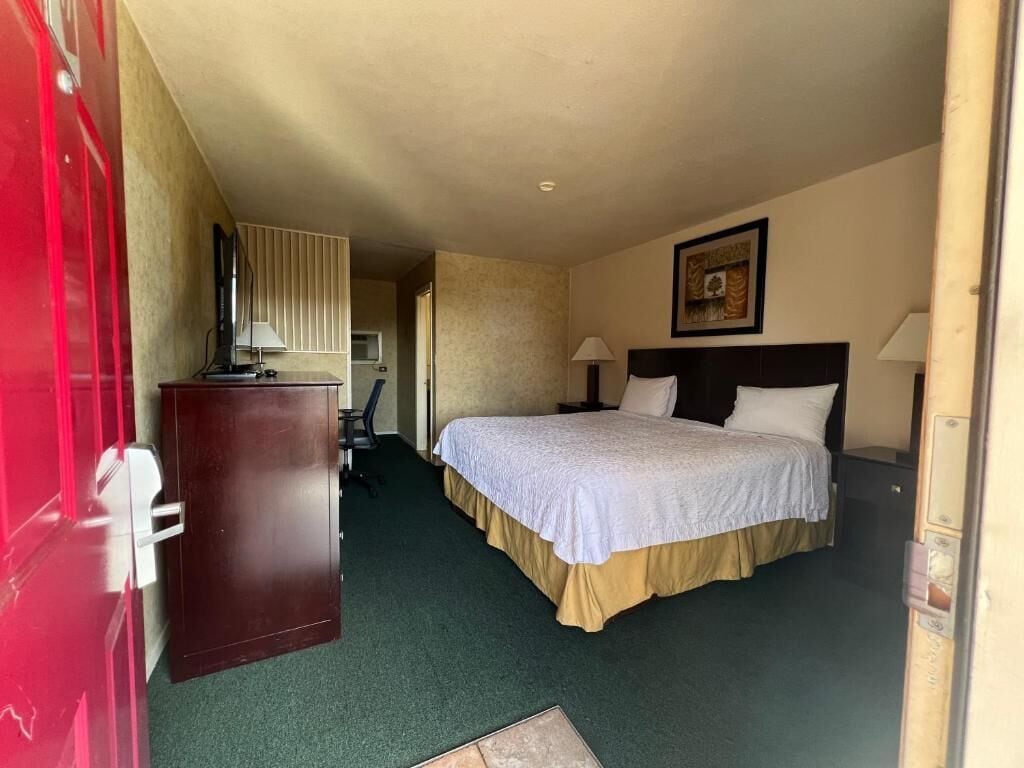 A hotel room with a bed, bedside lamps, a desk with a lamp, and a door.