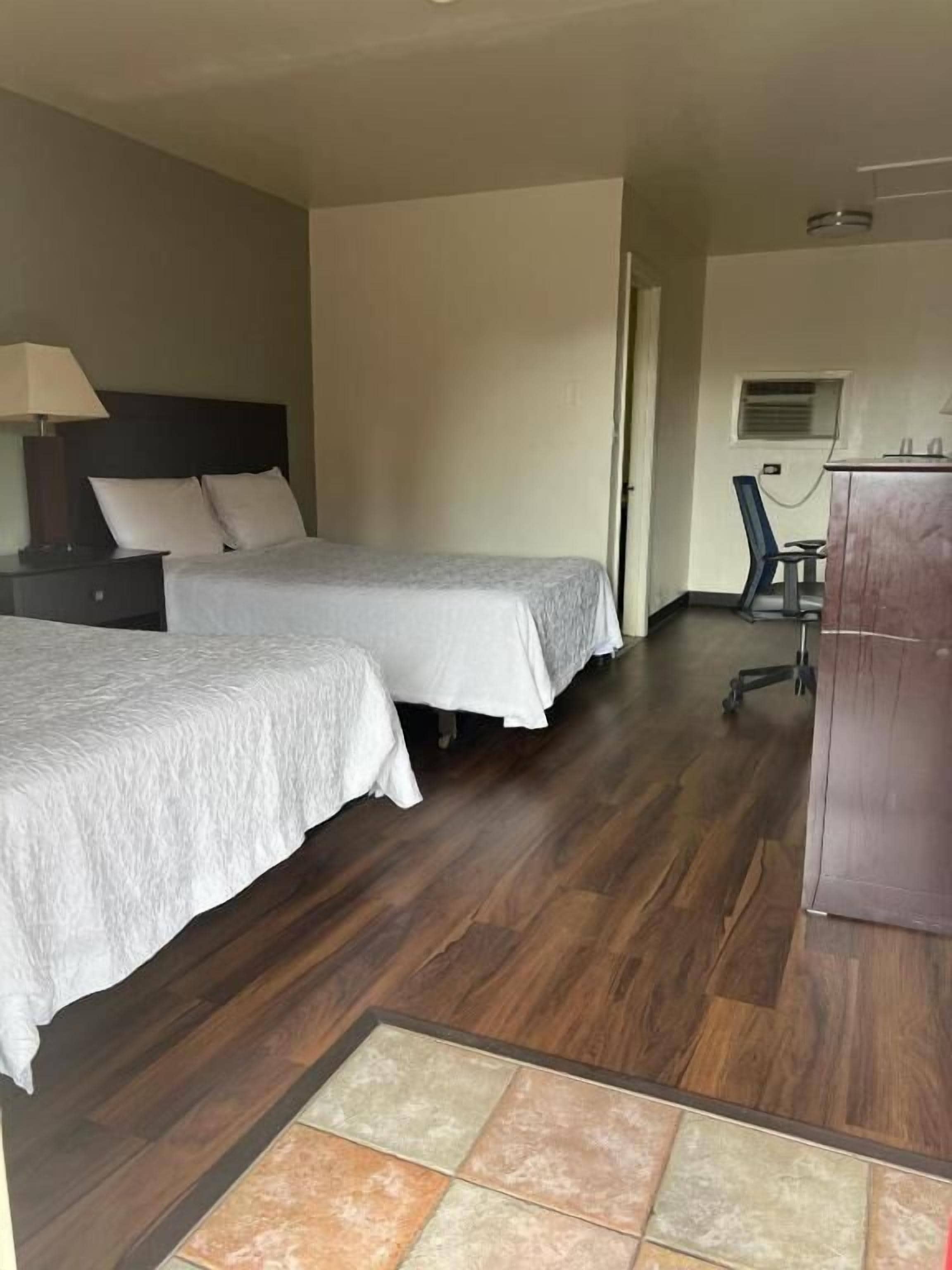 Habitación de hotel con dos camas, un escritorio, una silla, un armario y piso de baldosas.