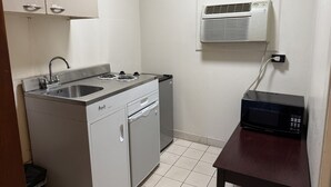 Una kitchenette compacta con estufa integrada, lavamanos y microondas sobre una pequeña mesa.