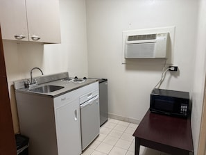 Una kitchenette compacta con estufa integrada, lavamanos y microondas sobre una pequeña mesa.